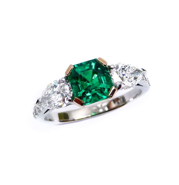 Emerald and diamond three stone ring, centred by a square trap cut emerald